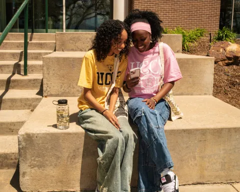 Two girls looking at a phone together in a pink and yellow UCCS shirts